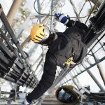 An electrician working on pipes and wiring on the high ledge of a building