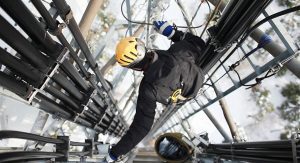 An electrician working on pipes and wiring on the high ledge of a building