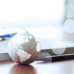 A small globe, a notebook with reading glasses on top, and a pen sitting on a desk