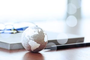 A small globe, a notebook with reading glasses on top, and a pen sitting on a desk