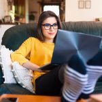 Female home worker sitting on the couch with her legs on the table and a computer on her lap