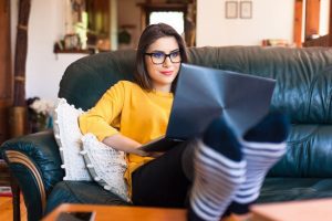 Female home worker sitting on the couch with her legs on the table and a computer on her lap