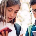 Huddle of children with backpacks and texting on their smartphones