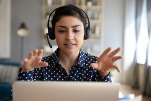 Person wearing headphones with hands up at computer screen