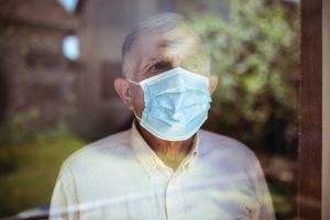 Older man wearing a COVID-19 mask staring out of the window