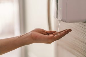 A hand placed under the automatic hand sanitiser dispenser.
