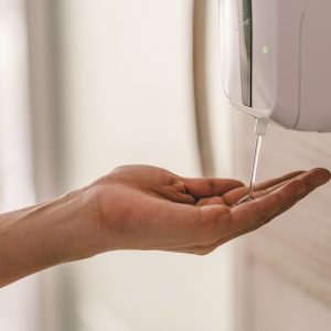 A hand placed under the automatic hand sanitiser dispenser.