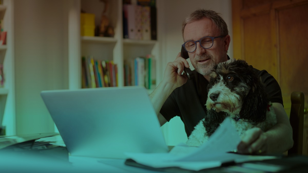 A man working from home taking a phone call while his dog sits on his lap.