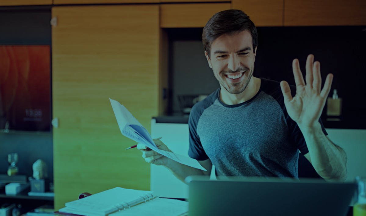 A happy man working from home with a laptop waving his hand.