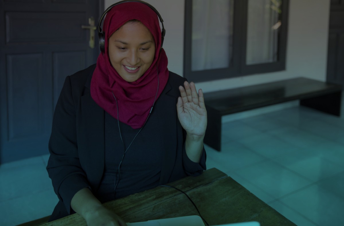 A woman working from home with her headphones on and waving her hand.