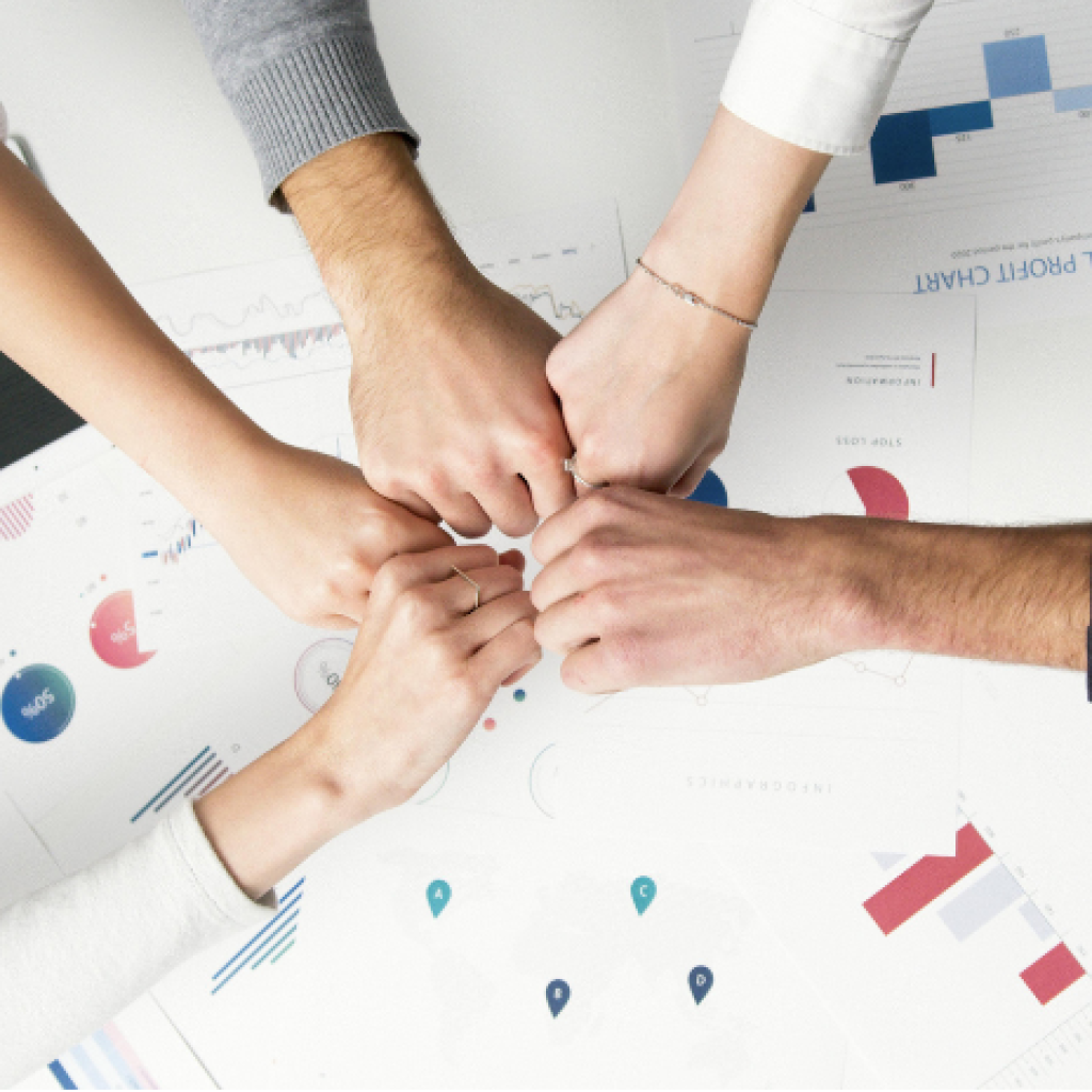 A team of workers fist bumping over data sheets.