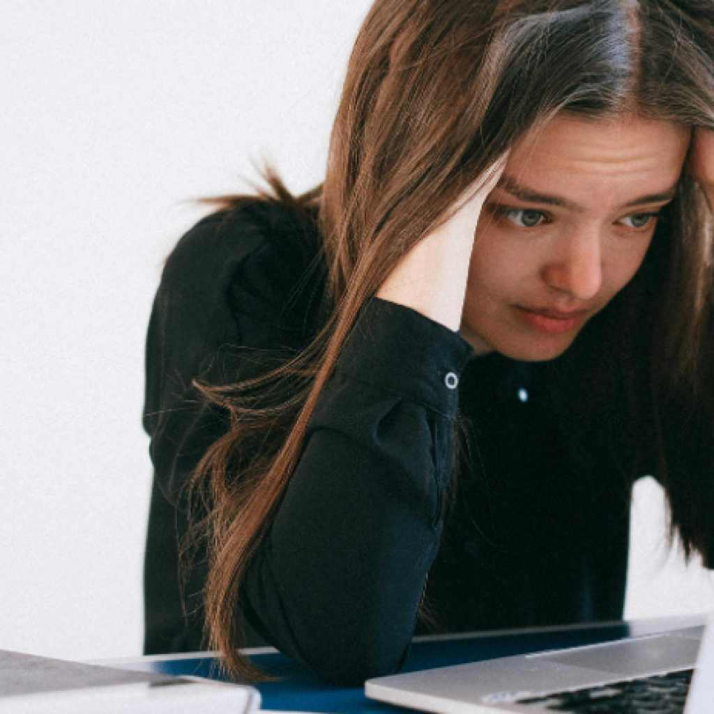 A worried-looking worker holding her head in her hands at her computer.