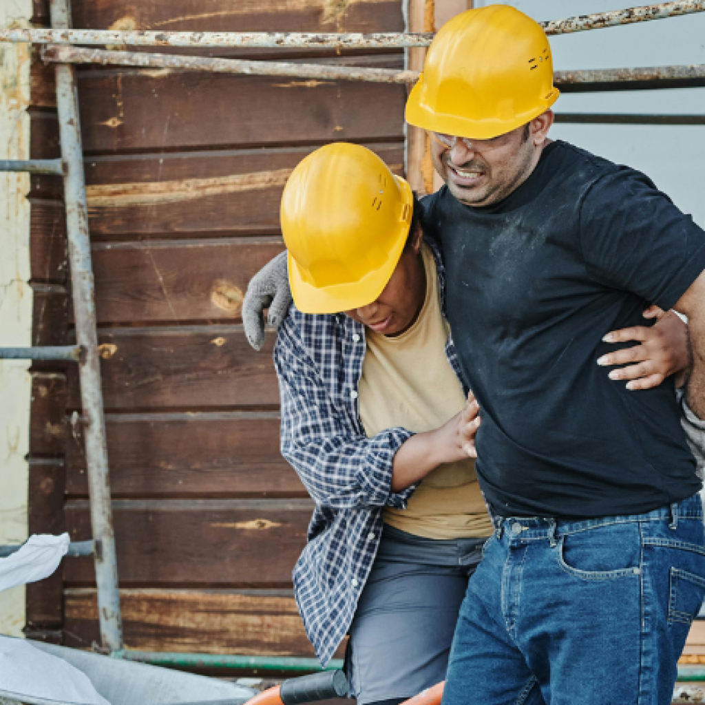 A builder supporting their colleague who has just sustained a back injury on the job