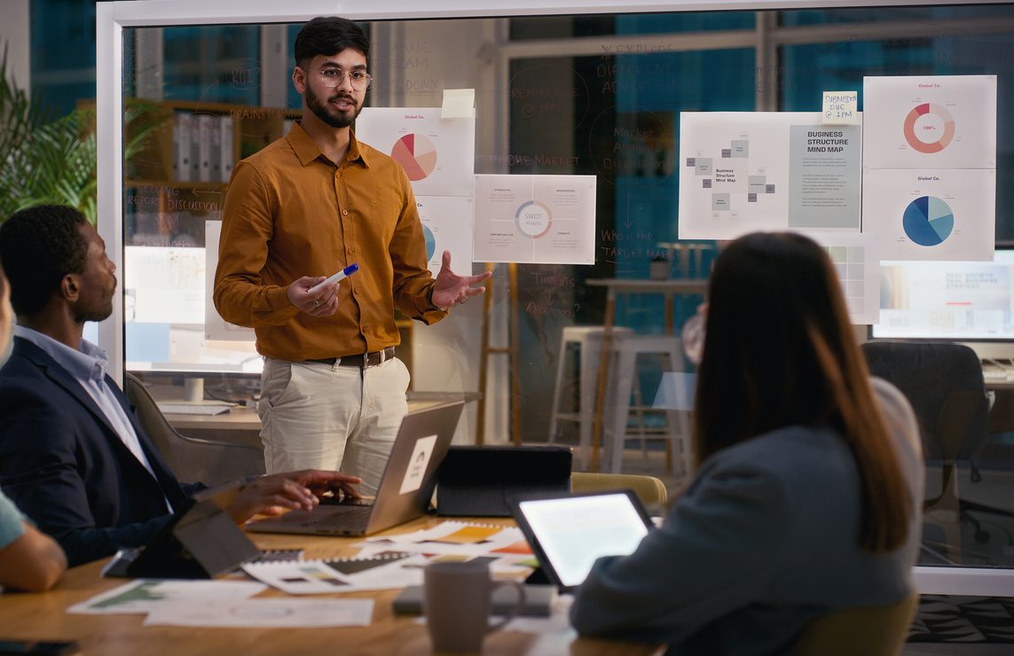 Creative business people, night and man in presentation for meeting, ideas or strategy at office. Staff, speaking or group of designers talking in team collaboration or sharing startup data analytics