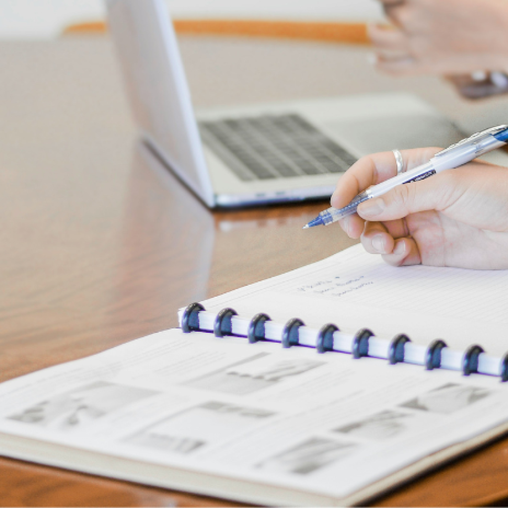 Someone filling out a report at a desk next to someone else using a laptop