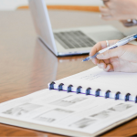Someone filling out a report at a desk next to someone else using a laptop