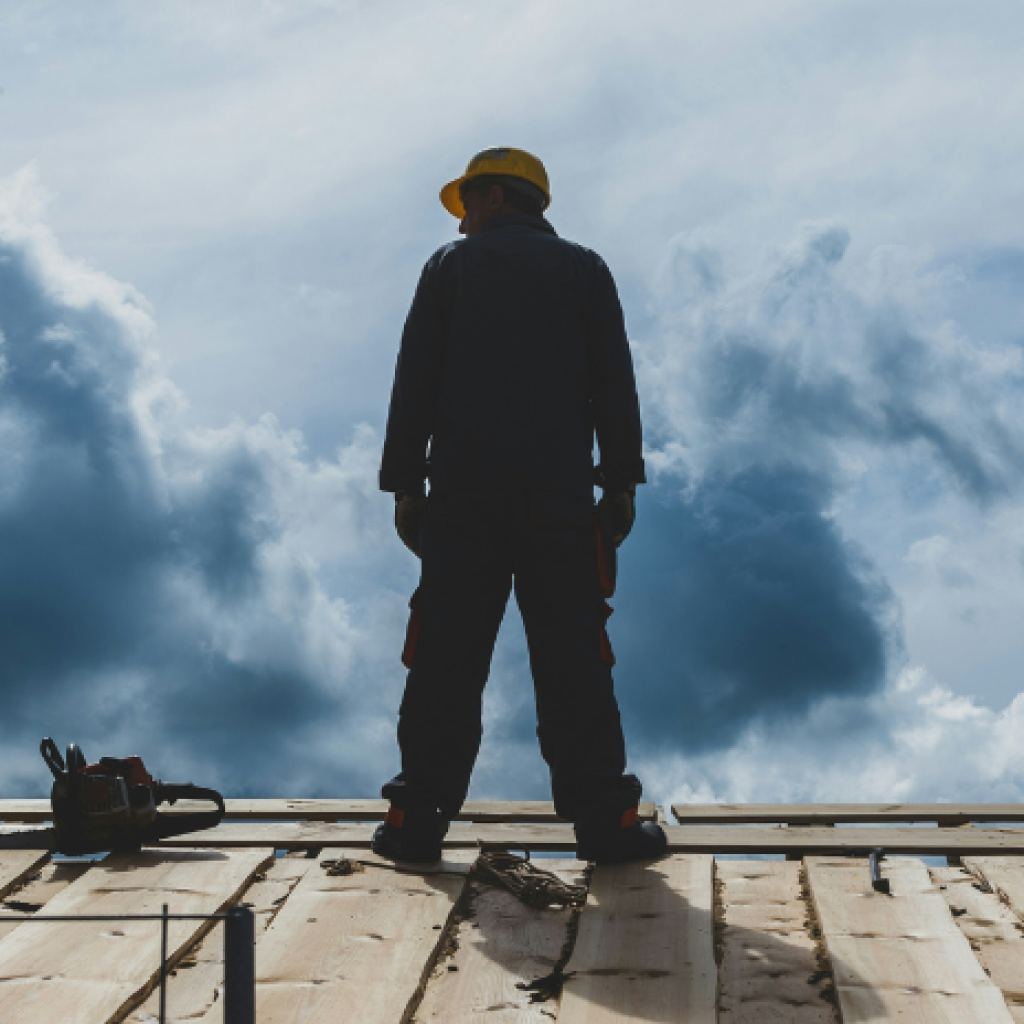A lone worker in a hard hat looking out in a bank of clouds from a platform