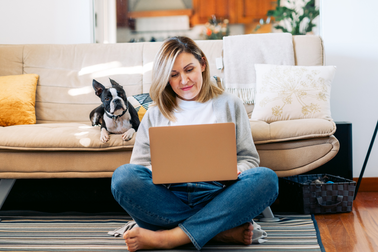 Young woman working from home with a boston terrier dog. Freelancer businesswoman using laptop at sunny room. Student learning and working at home.
