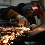 A manufacturing professional sawing through a sheet of metal, with sparks flying towards the bottom-left side of the image
