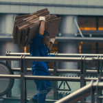 An industrial worker carrying a stack of flattened boxes above their head
