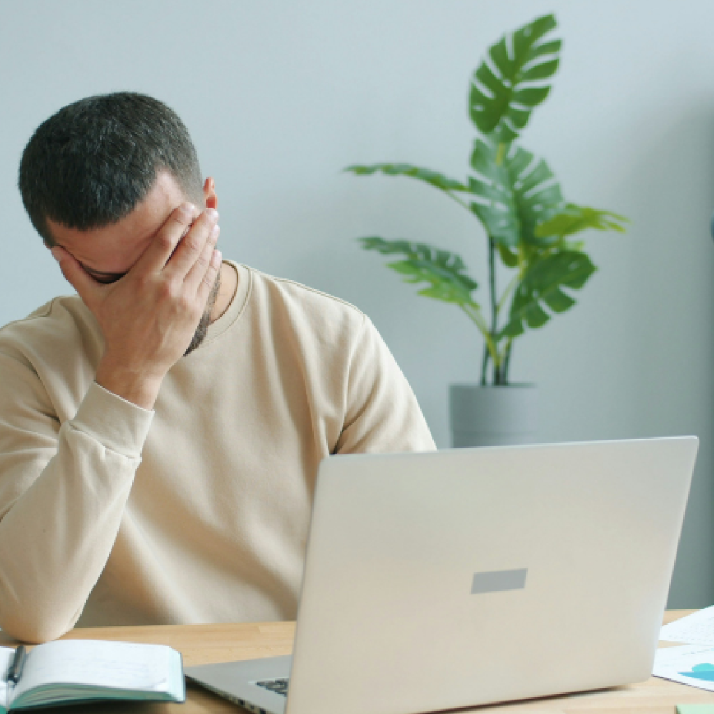 A knowledge worker experiencing digital fatigue at their computer desk - holding their hand over their eyes.