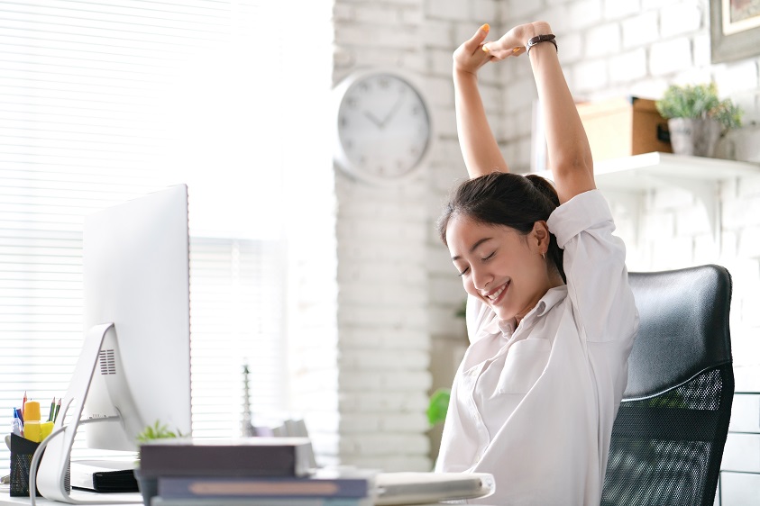 Lady stretching her arms above her head while sitting at her desk
