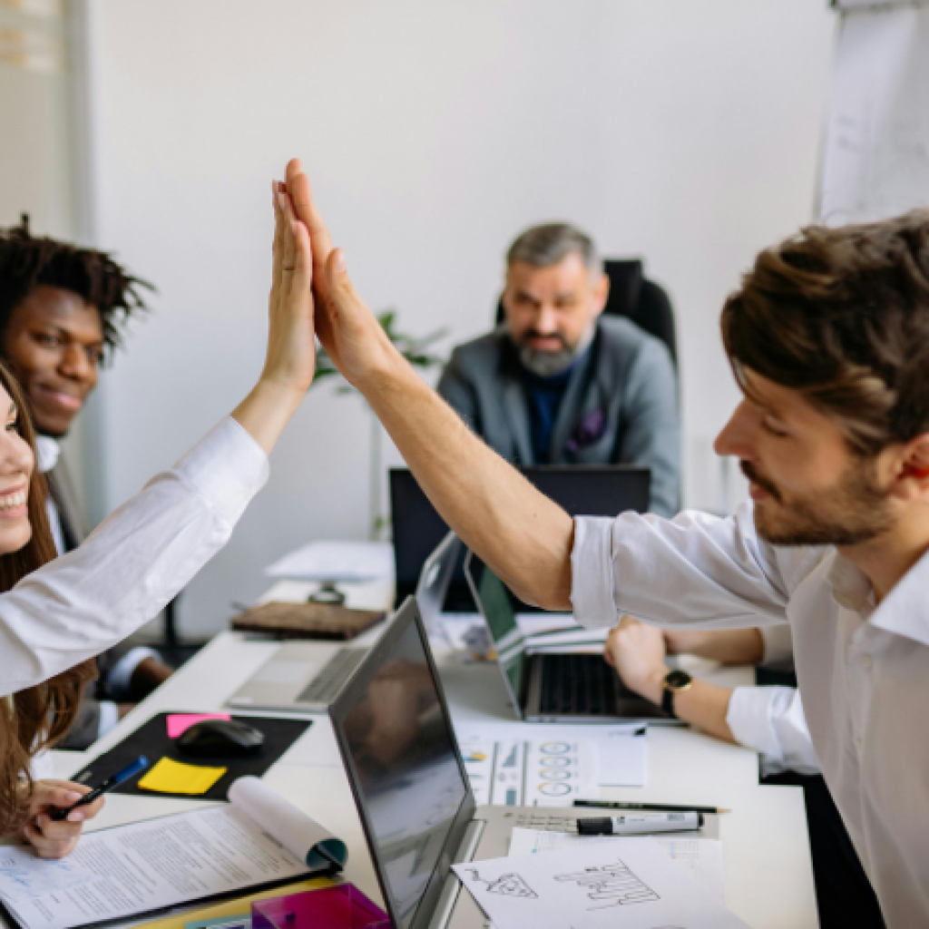 Office workers high-fiving in celebration during a team meeting.