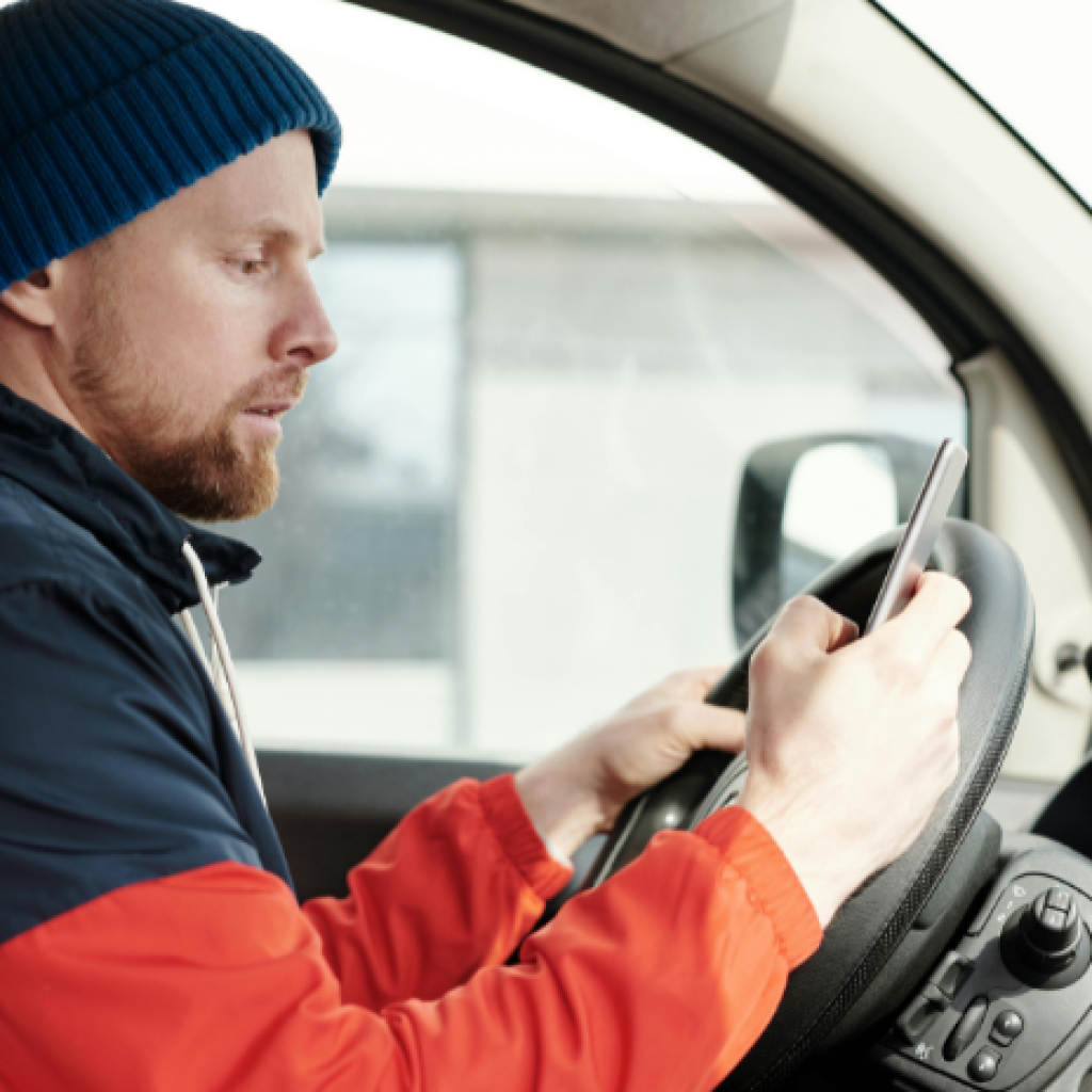 A delivery driver in a parked van looking at their smartphone.