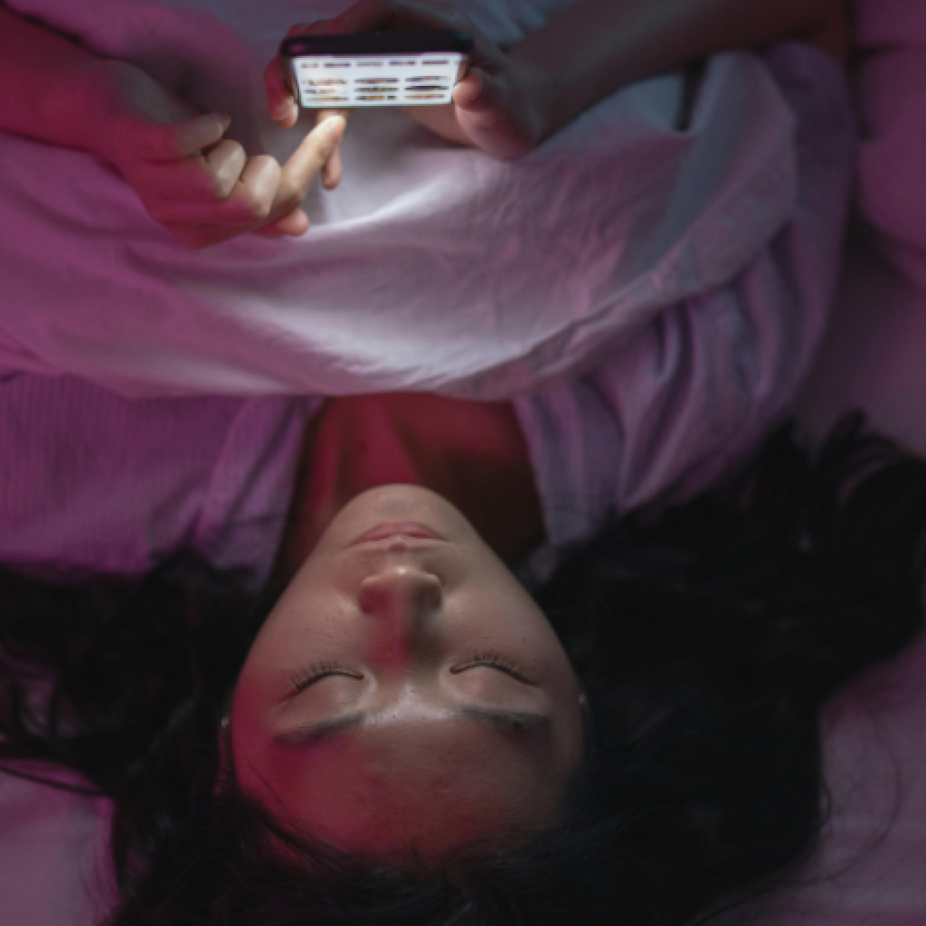 A person scrolling on their phone in bed at night.