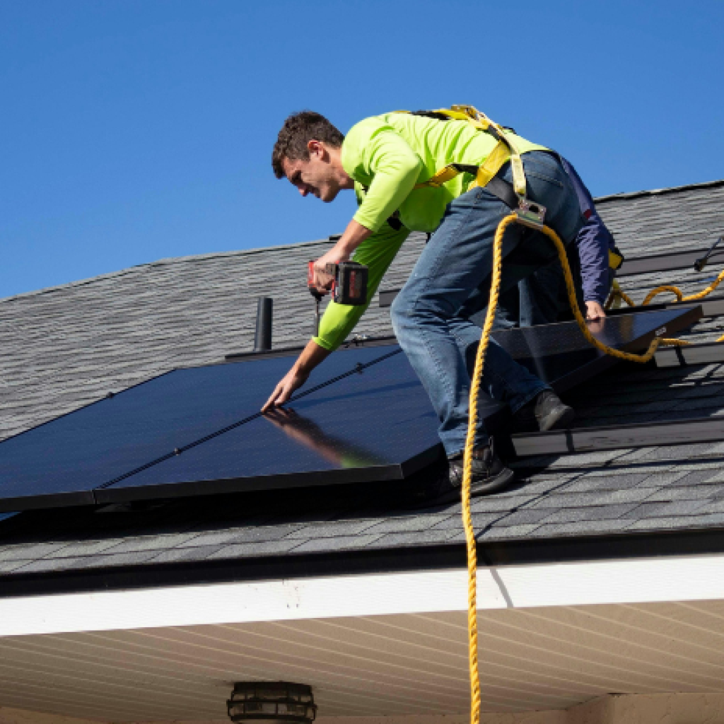A man harnessed on a roof, installing solar panels