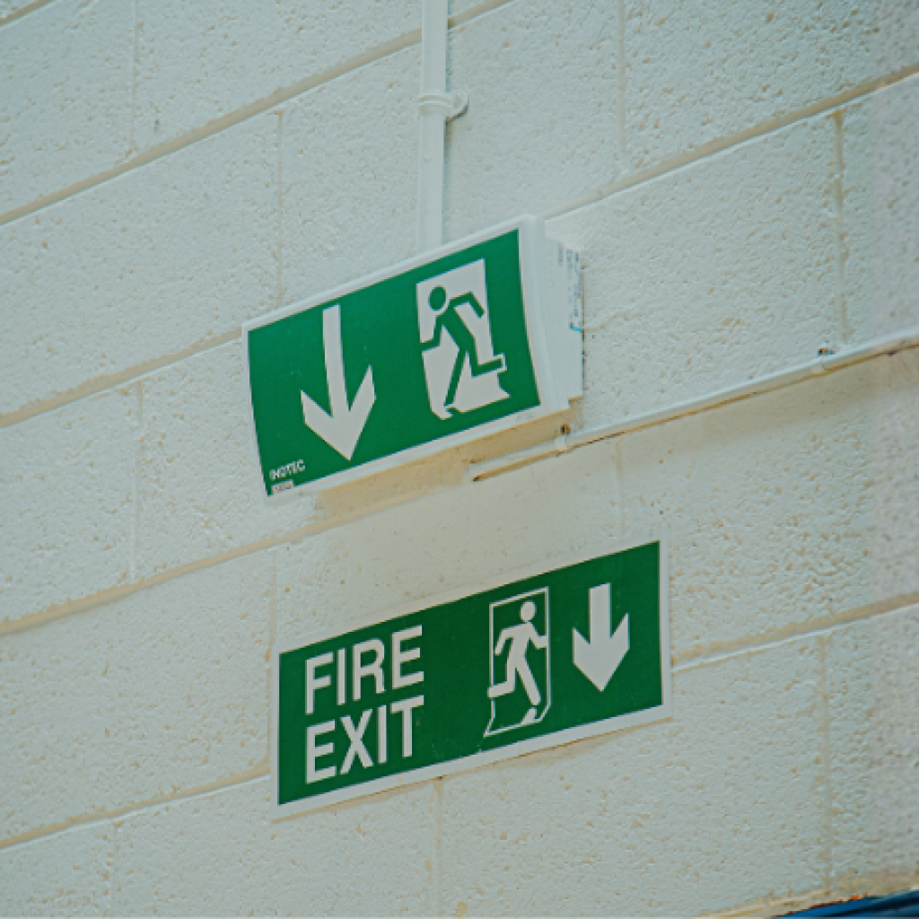 Fire Exits signs installed on a white wall above a fire exit