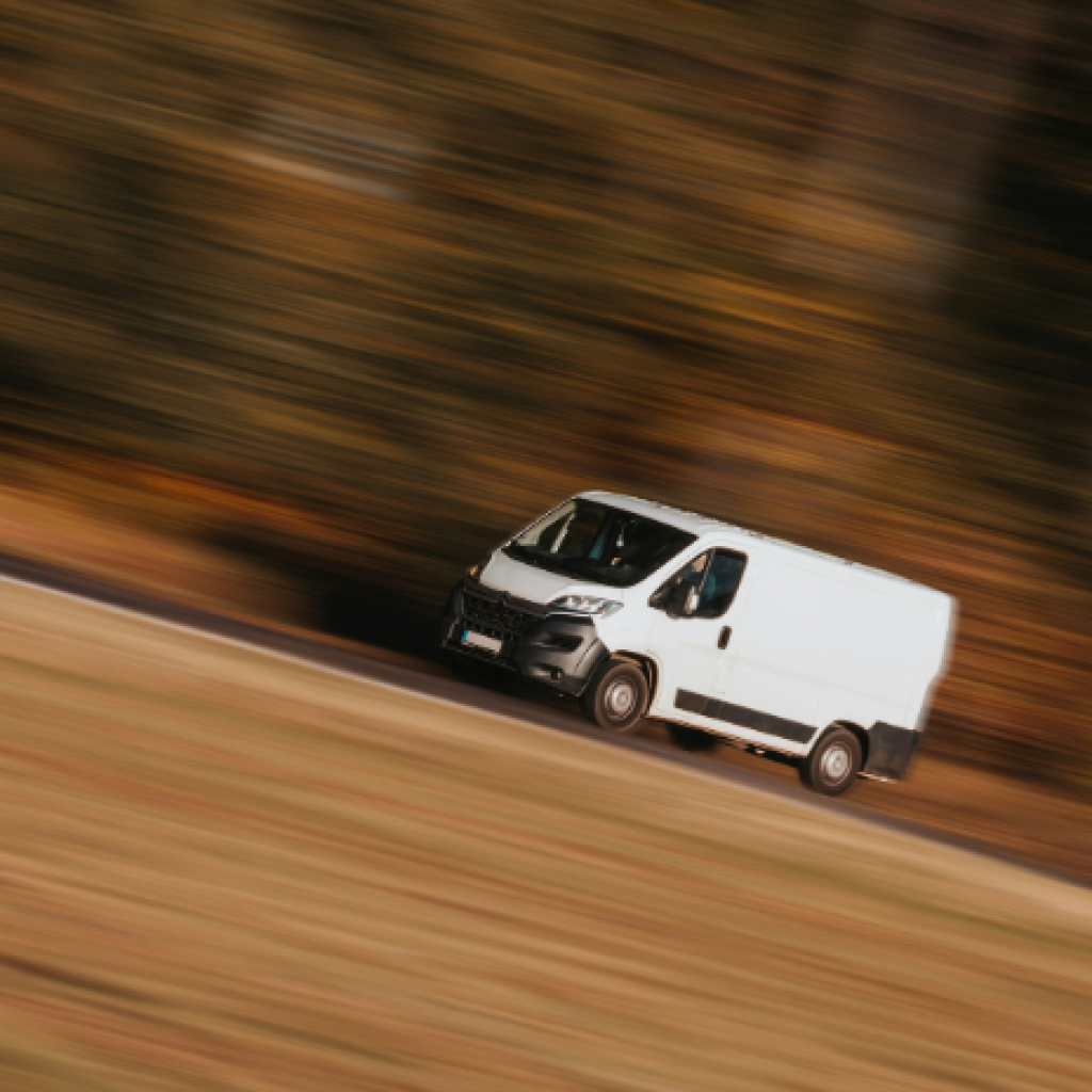 A white delivery van travelling at pace along a hillside road.