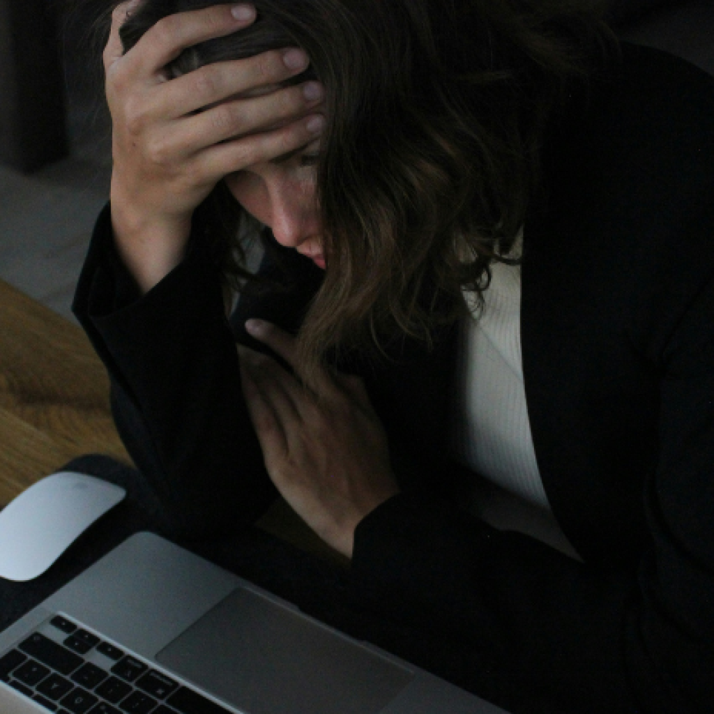 A stressed worker looking at her laptop will holding a hand to her head.