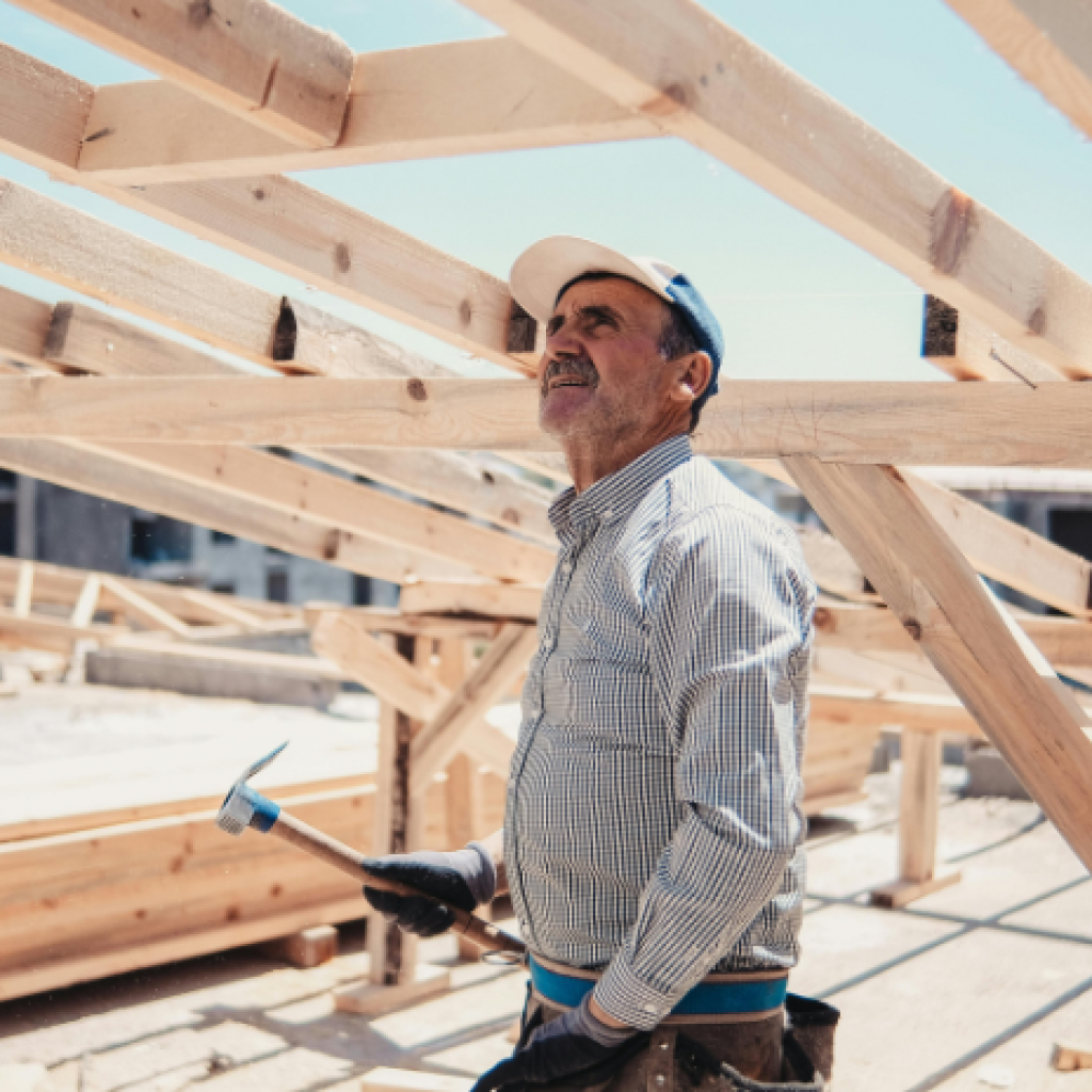 An older construction worker assessing a roof frame on a sunny day