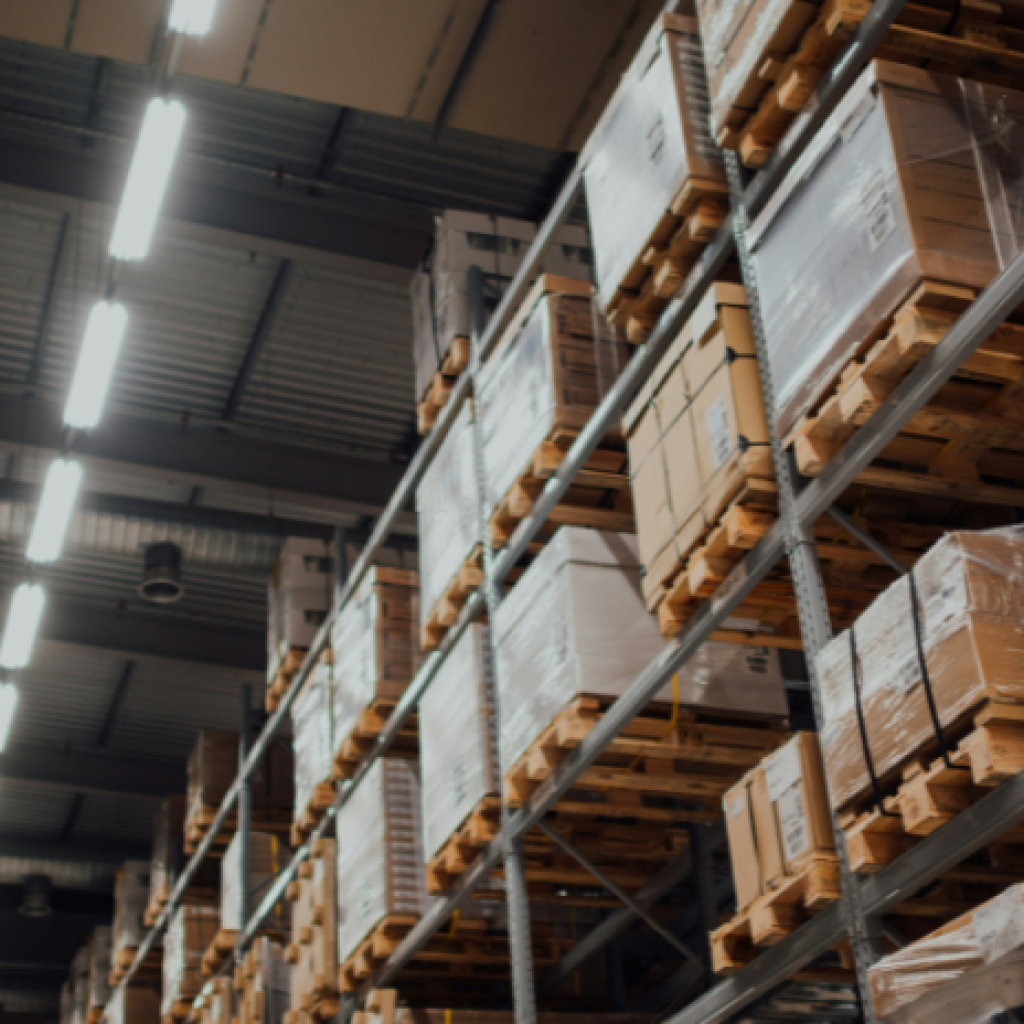 A view of the top of a warehouseing shelf unit and lighting overhead - as seen from the vantage point of someone waling in the aisle.